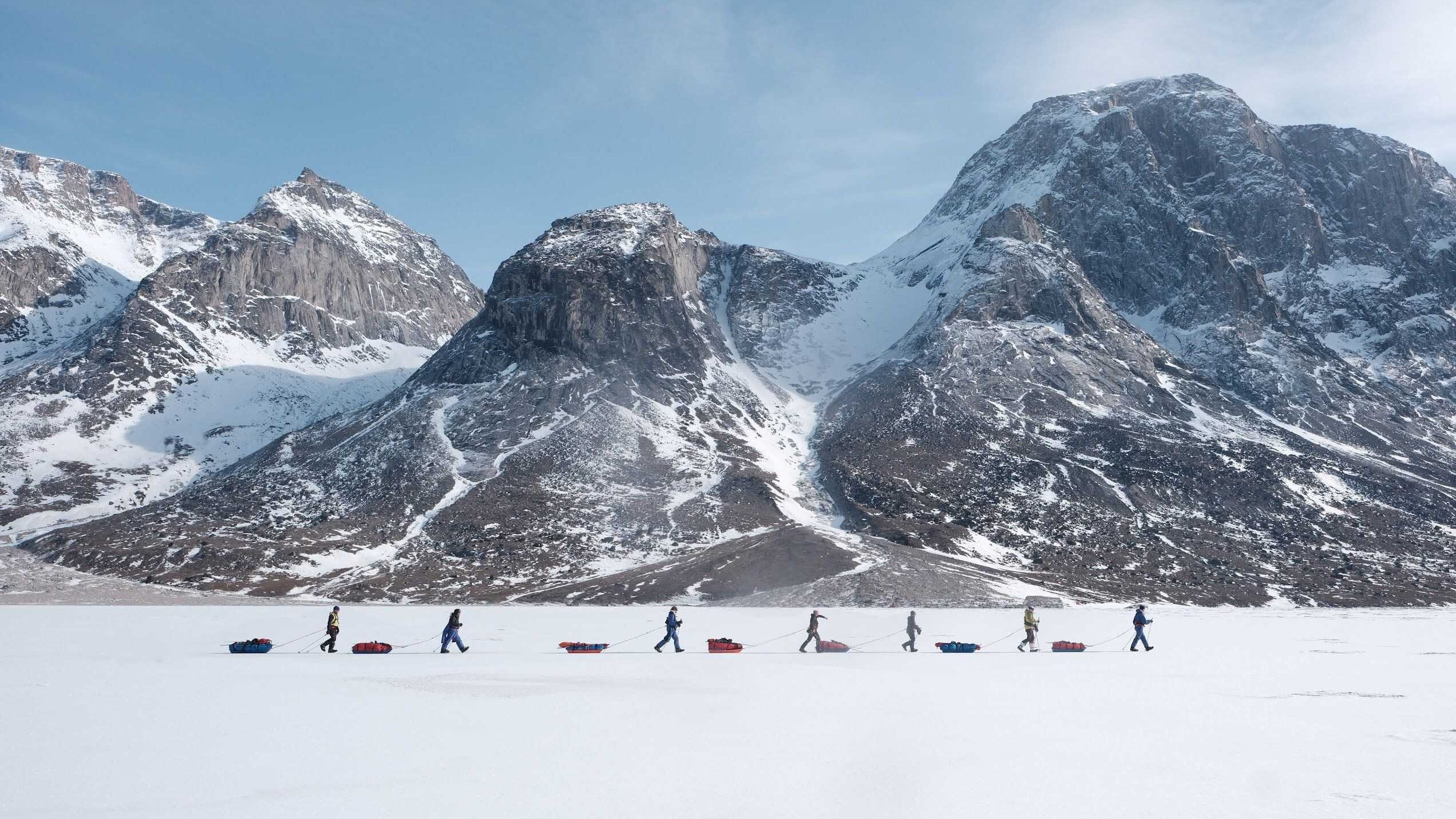 A group of people walking in the snow pulling pulks