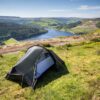 Laser Compact AS (2) Small dark backpacking tent pitched on a grassy hilltop overlooking a winding blue reservoir and green rolling hills under a clear sky.