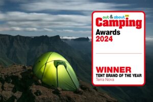 Green illuminated dome tent pitched on a rocky mountain ledge at night under a cloudy sky, next to a red‑bordered badge reading “out & about Camping Awards 2024 — WINNER: Tent Brand of the Year Terra Nova.”