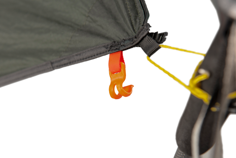 Close-up of an orange plastic hook clipped to a red webbing loop on the corner of a dark green tent fly, with a yellow guyline attached to a black strap and a tent pole visible at the right