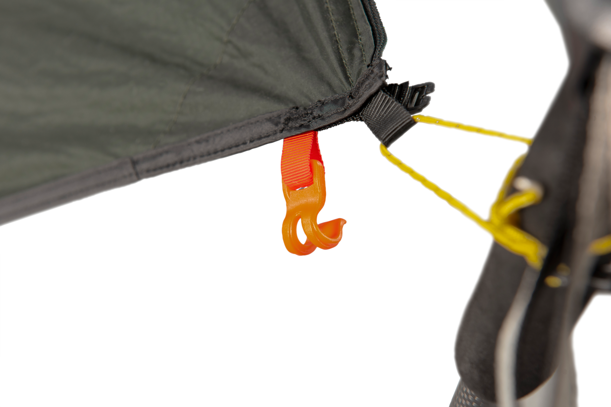 Close-up of an orange plastic hook clipped to a red webbing loop on the corner of a dark green tent fly, with a yellow guyline attached to a black strap and a tent pole visible at the right