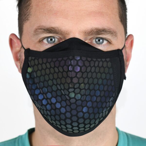 23MRFM-Maze-Runner-Face-Mask-Worn-Daylight-1500x1500px-1.jpg Close-up of a man wearing a black cloth face mask with an iridescent hexagonal honeycomb pattern, showing his light blue eyes and short dark hair against a plain background.