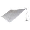 43TU1-Ultra-tarp-1-back-view-square-1.jpg Silver rectangular tarp shelter with reinforced attachment points and a small brand label, pegged at three corners and tensioned on the right by a walking pole and guy line.