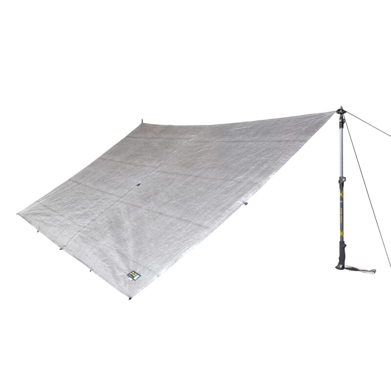 43TU1-Ultra-tarp-1-back-view-square-1.jpg Silver rectangular tarp shelter with reinforced attachment points and a small brand label, pegged at three corners and tensioned on the right by a walking pole and guy line.