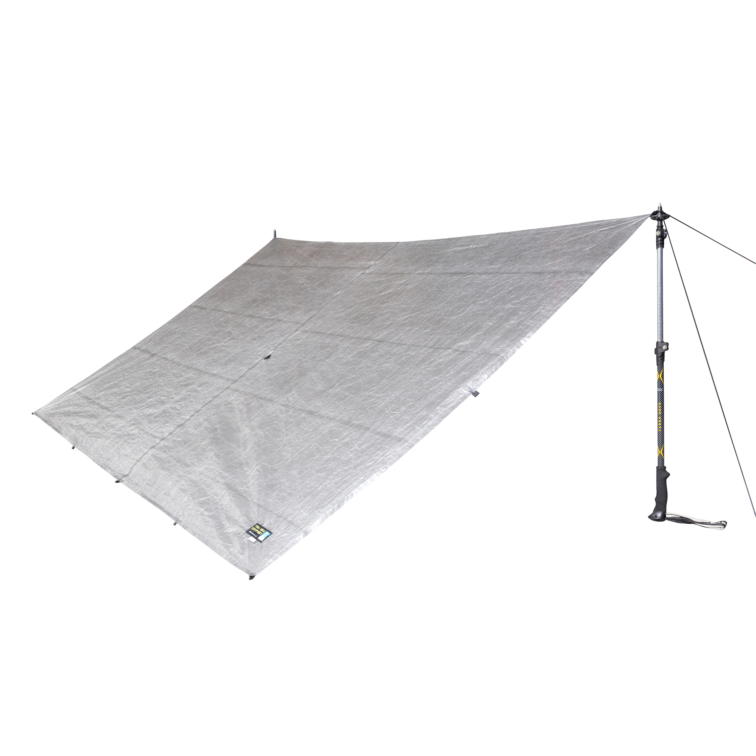 Silver rectangular tarp shelter with reinforced attachment points and a small brand label, pegged at three corners and tensioned on the right by a walking pole and guy line.