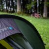 BenReadPhotography_Bikepacking-6-scaled-2.jpg Close-up of a rain-speckled green and grey Terra Nova Equipment Starlite tent fly pitched on wet grass, with a blurred red bicycle and trees in the background.