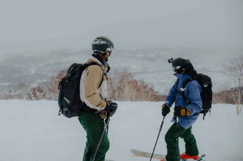 Capitol Peak & Torres Peak Two skiers in winter gear standing on a snowy mountain slope, preparing for a run amidst a foggy landscape.