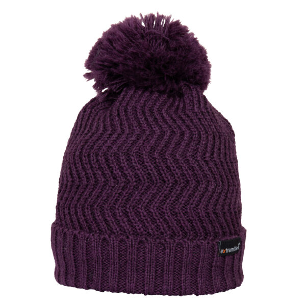 Deep purple knitted beanie with a large fluffy pom-pom, chevron zigzag stitch pattern, ribbed folded cuff and small black brand label on the brim.