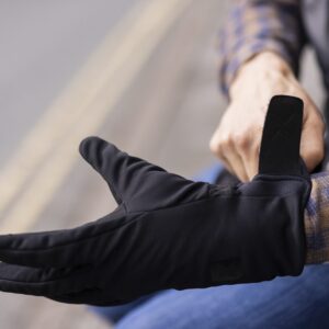 Close-up of a person fastening the Velcro strap of a black glove over their wrist while wearing a blue-and-brown checked shirt, with blurred road lines in the background.