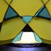 Interior view of a yellow and teal camping tent with triangular mesh panels and an open low doorway revealing grass outside