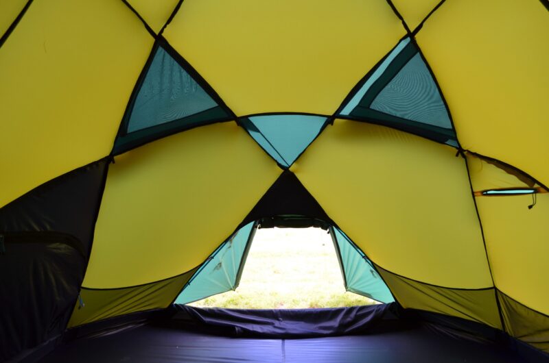 Interior view of a yellow and teal camping tent with triangular mesh panels and an open low doorway revealing grass outside