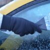DSC_0645-scaled-2.jpg Black-gloved hand in a cream knit sleeve using a triangular plastic ice scraper to remove frost and ice from a car side window with the yellow car body visible.