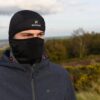 DSC_5133-scaled-2.jpg Person outdoors wearing a black thermal cap with an 'extremities' logo and a matching face mask covering the lower face, dressed in a zipped dark grey jacket against a blurred grassy and wooded landscape.