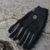 EXTREMITIES_PHOTOGRAPHY_2023_0143-3.jpg Black lightweight gloves with grey fingertip panels and a small logo, laid flat on a rough grey stone surface