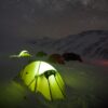 Expedition-Quasar-Lifestyle-3.jpg Glowing yellow-green tent in the snowy foreground with several other tents pitched on a snow-covered mountain slope beneath a clear, star-filled night sky and distant peaks.