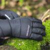 Extremitieshoot_Oct2019-141-scaled-2.jpg Black padded extremities glove lying palm-down on bright green moss with a red jacket cuff visible at the wrist.