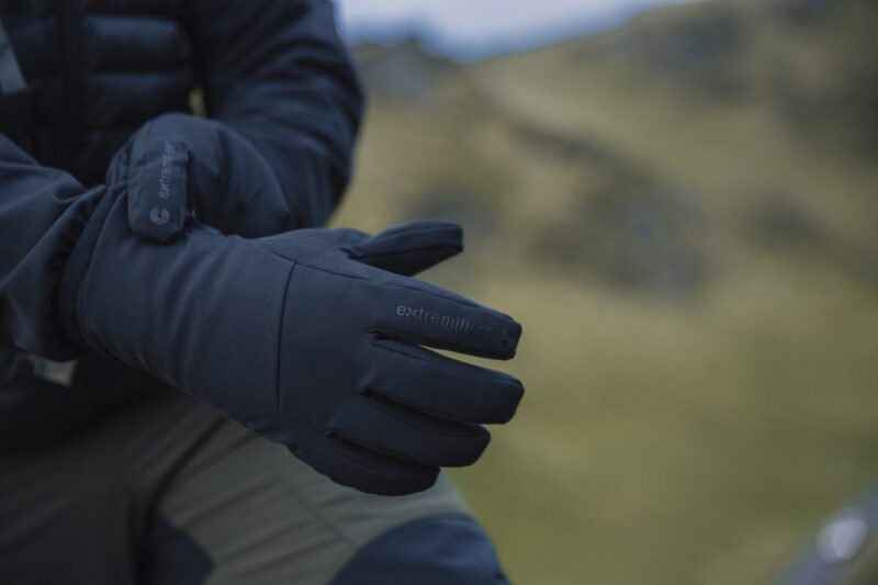 Focus-Glove-1-3.jpg Close-up of a person adjusting dark insulated Extremities gloves with a blurred grassy hillside in the background.