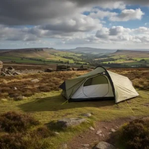 Scenic view of a camping tent set up on a grassy hillside, surrounded by rocky formations and rolling green fields under a cloudy sky, ideal for outdoor enthusiasts and nature lovers.
