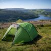Halcyon-2-1-1.jpg Small green tent pitched on a grassy hillside overlooking a reservoir with a dam and arched bridge, surrounded by wooded slopes and rolling green fields under a clear blue sky.