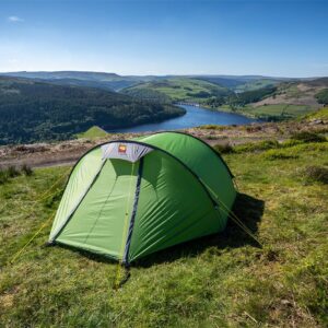 Green dome tent pitched on a grassy hillside overlooking a blue reservoir and rolling patchwork hills under a clear blue sky.