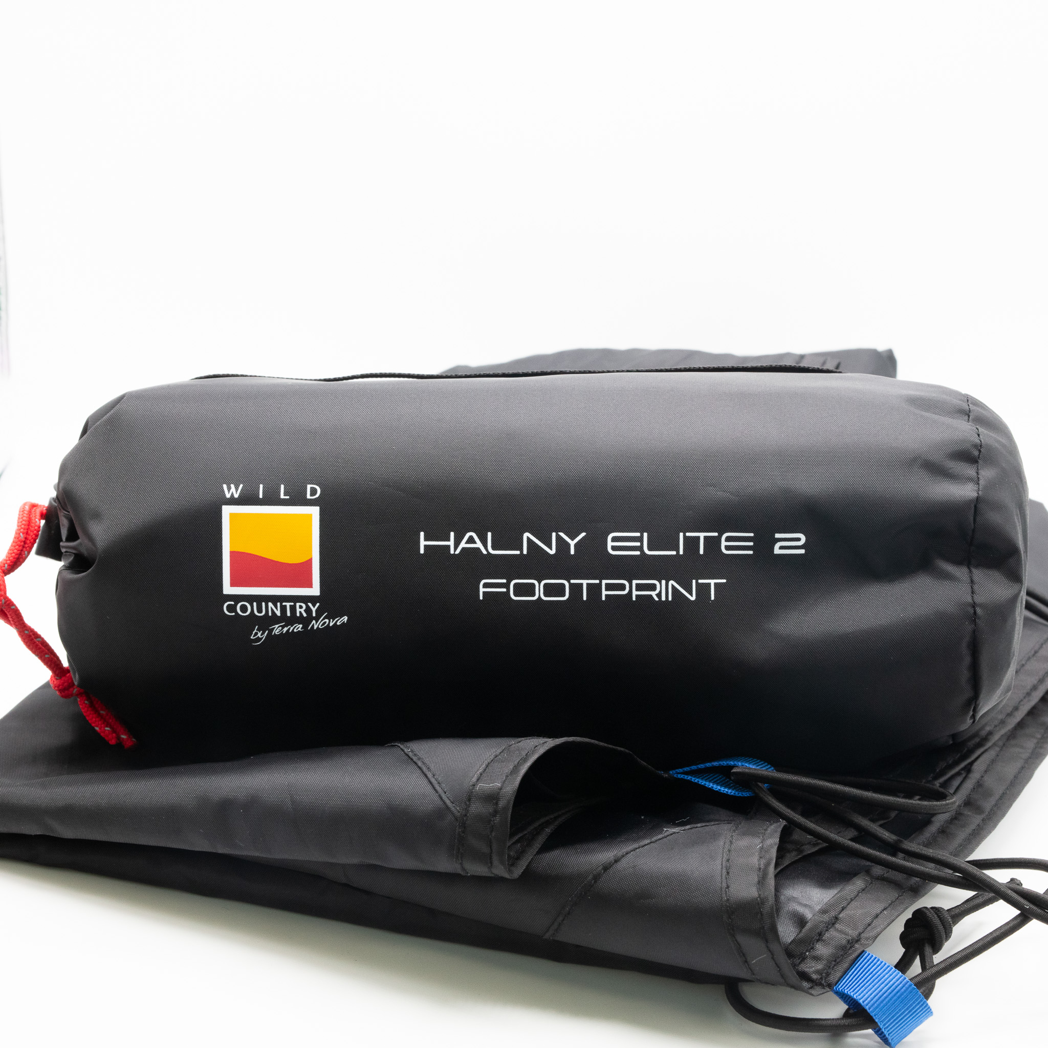 Halny-Elite-2-2-3.jpg Black cylindrical storage bag marked "WILD COUNTRY" and "HALNY ELITE 2 FOOTPRINT", cinched with a red cord and resting on folded black tent fabric.