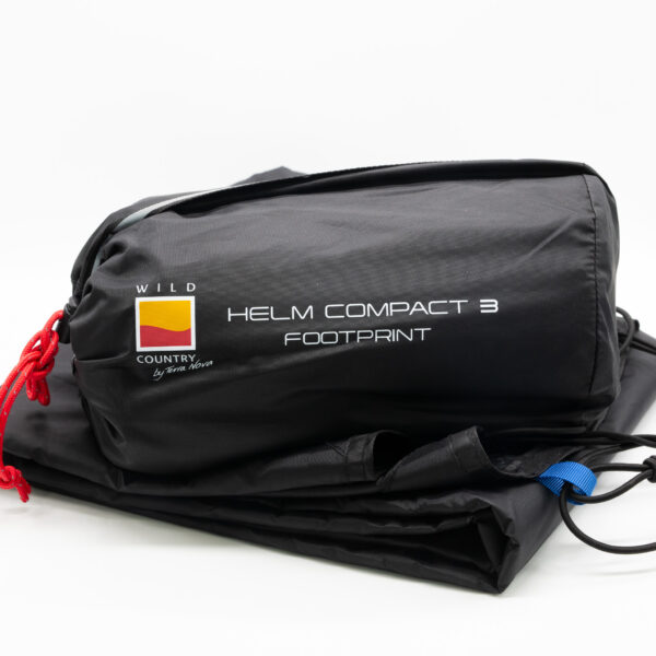 Black storage bag labeled HELM COMPACT 3 FOOTPRINT with Wild Country logo, red drawcord and blue tab, containing a folded tent footprint on a white background.