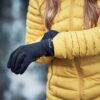 LIN-TERRANOVA-211109-2280-scaled-2.jpg Person wearing a yellow puffer jacket sliding on black winter gloves, hands and jacket in sharp focus against a blurred outdoor background.