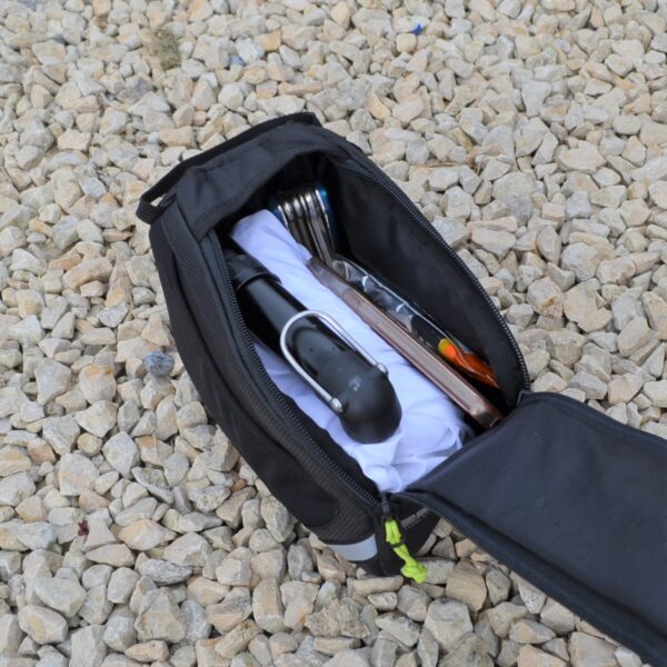 Laser-Velo-Frame-With-Contents-1.jpg Open black zippered pouch resting on pale gravel, containing a folded white cloth and assorted cycling tools — a compact hand pump or mini lock with a curved metal bracket, a multi-tool with folded hex keys and an orange tyre lever.