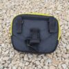 Laser-Velo-Handlebar-Attachment-Points-1.jpg Small rectangular black fabric pouch with yellow trim, two vertical belt loops and a central velcro strap visible on its back, lying on a bed of pale gravel.