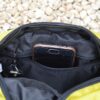 Laser-Velo-Handlebar-Inside-Pocket-Close-Up-1.jpg A black smartphone in a clear protective case sticks out of a zippered inner pocket of a yellow fabric pouch, a key on a ring peeks from the pocket and pale gravel is visible in the background.
