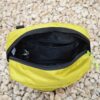 Laser-Velo-Handlebar-Inside-View-1.jpg Top-down view of an open yellow-green zippered pouch with black interior lining, an internal zip pocket and key clip, resting on pale gravel.