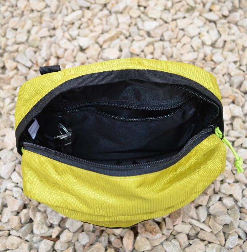 Laser-Velo-Handlebar-Inside-View-1.jpg Top-down view of an open yellow-green zippered pouch with black interior lining, an internal zip pocket and key clip, resting on pale gravel.