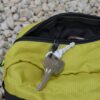 Laser-Velo-Handlebar-Key-Attachment-1.jpg Silver house key on a small keyring lies on a partially open lime-green zippered pouch, with a smaller key and black zipper visible against pale gravel.