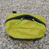 Laser-Velo-Handlebar-Top-Zips-1.jpg Top-down view of a small lime-green ripstop zippered pouch with black trim and neon-green cord zipper pulls resting on pale gravel stones.