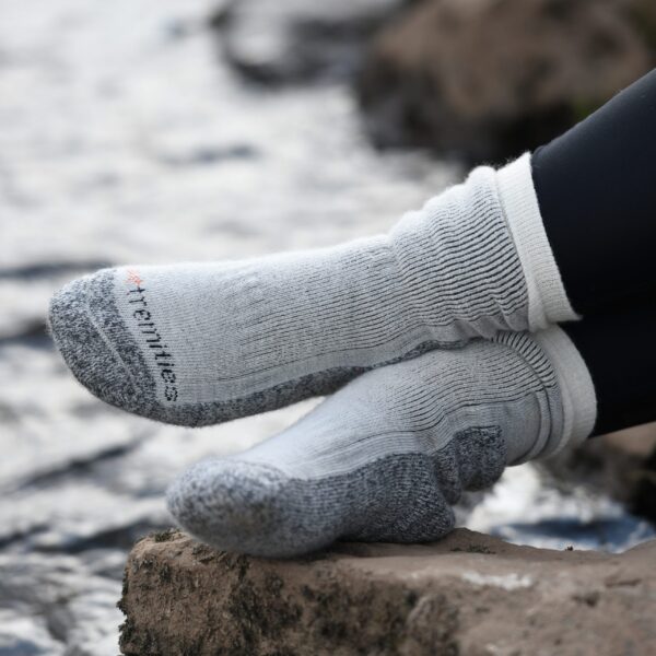 Mountain-Toester-26MTO-3000x3000px-300dpi-scaled-4.jpg Feet in thick light-grey ribbed socks with dark-grey reinforced toes and heels, legs in black leggings, resting on a rock beside a blurred flowing stream.