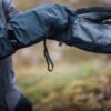 Mountain_Mitt_LS-5-scaled-4.jpg A person wearing dark waterproof mittens with leather palms and adjustable wrist straps, hands extended against a blurred grassy outdoor background.