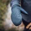 Mountain_Mitt_LS-scaled-4.jpg Close-up of an outstretched padded teal mitten showing visible stitching, worn with a dark jacket against a blurred outdoor background.