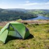 Panacea-2-2-With-logo-3.jpg Green two-person dome tent pitched on a grassy hilltop overlooking a reservoir with a forested ridge, arched stone bridge and patchwork green fields under a blue sky