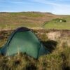 Pioneer-2-4-scaled-4.jpg Small green dome tent pitched in grassy moorland with rolling hills, a winding lane and a distant farmhouse under a clear blue sky.