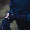 Power-Liner-Wrist-Gaiter-2-3.jpg Close-up of two hands adjusting black thumb-hole gloves with visible "extremities" branding over a dark waterproof jacket against a blurred outdoor background.