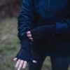 Power-Liner-Wrist-Gaiter-3-3.jpg Person outdoors wearing a navy jacket and black thumb‑hole gloves, adjusting one sleeve with their hands visible against a blurred grassy background.
