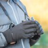 Quest-glove-lifestyle-1500x1500px-1.jpg Close-up of a person in a grey puffer jacket with black insulated gloves holding compact binoculars on a neck strap against a softly blurred golden outdoor background.