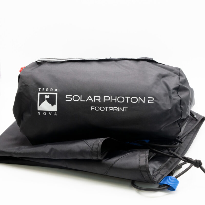 Solar-Photon-2-2-3.jpg Black packed storage bag printed with 'Terra Nova Solar Photon 2 Footprint' resting on folded black footprint fabric with a visible blue webbing pull tab and drawcord.