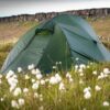 Solar-Photon-2-4-scaled-2.jpg A green dome tent pitched on grassy moorland dotted with white cotton-like flowers, with a low rocky escarpment in the background under a pale sky.