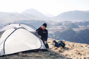 Man setting up a tent in a mountainous landscape, showcasing camping gear and outdoor adventure.