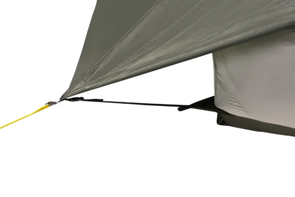 Close-up of a grey tent fly corner secured by a black webbing strap and yellow guyline to the tent base.