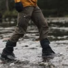 Tay-Ankle-GORE-TEX-Gaiter-24-LR-3.jpg Person's lower body in brown cargo trousers, black gaiters with orange drawcords and hiking boots stepping across a shallow rocky stream with water splashing around the boots