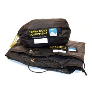 Black Terra Nova Equipment stuff sack with yellow logo patch and small mountain icon sitting on a folded black waterproof sheet showing brass grommets and a knotted drawcord