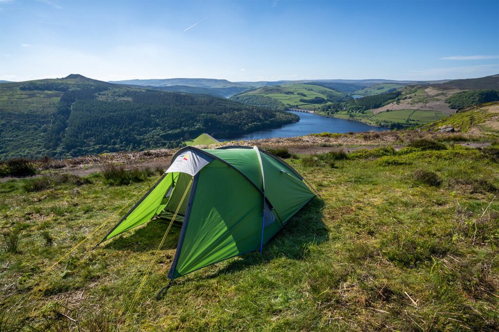 Trident-2-LR-1.jpg Green backpacking tent pitched on a grassy hilltop overlooking a blue reservoir with a dam and forested, rolling hills under a clear blue sky.