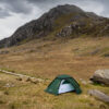 Terrs Nova Snowdonia Photography Shoot May 2023 Green dome tent pitched on grassy moor beside a large boulder in a broad, rocky mountain valley with steep crags rising in the background under an overcast sky.